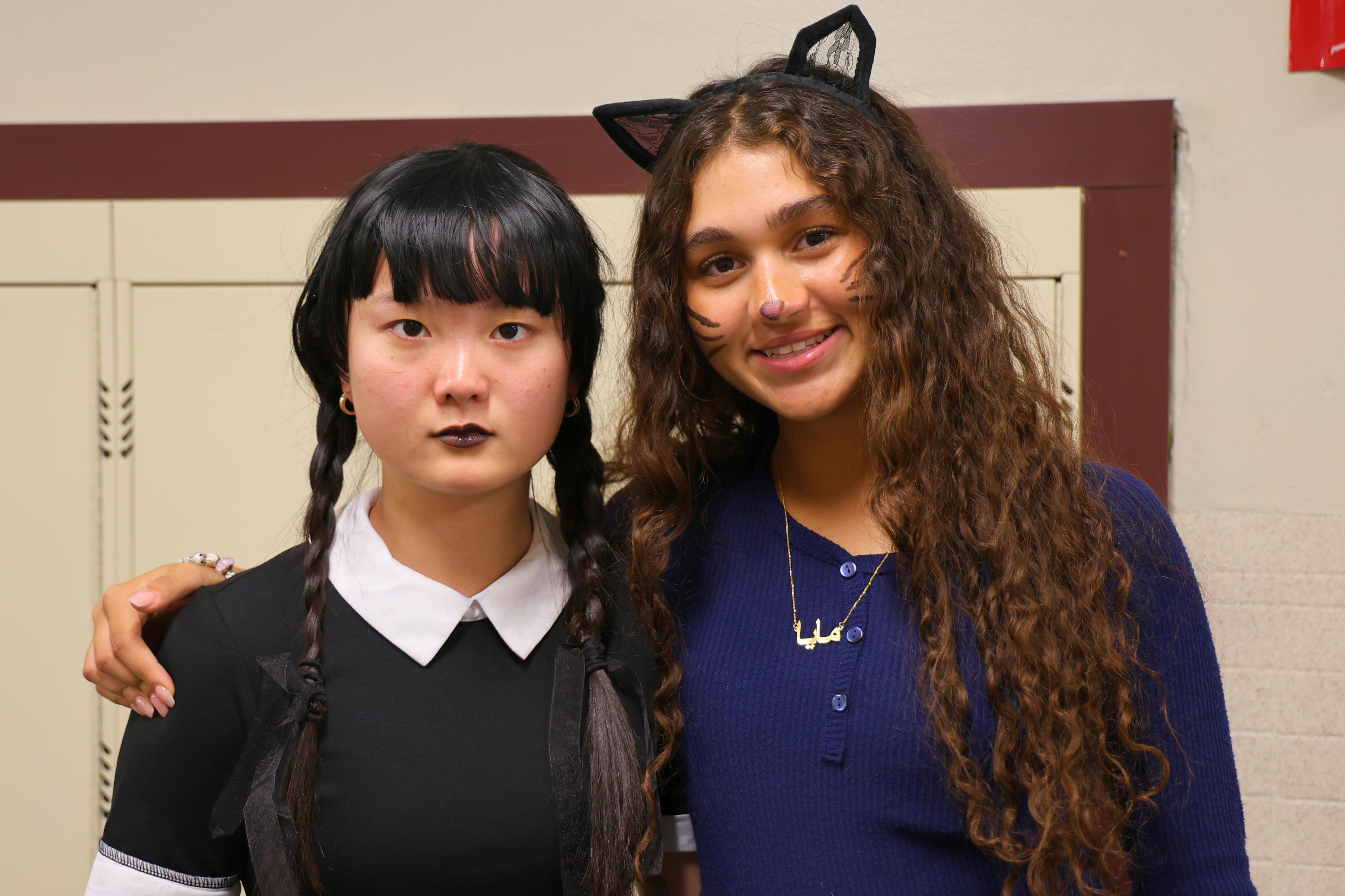 Two students dressed in halloween costumes pose for a picture in a hallway